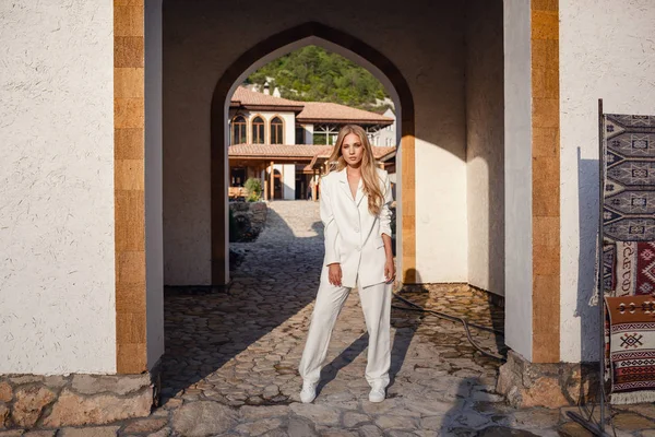 Outdoor full body fashion portrait of fashionable woman in white suit posing in street of east city — Stok fotoğraf