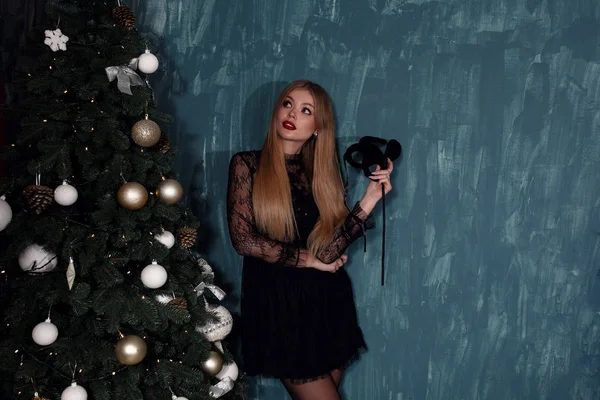 Όμορφη αισθησιακή γυναίκα με ξανθά μαλλιά σε πολυτελές μαύρο φόρεμα ποζάροντας δίπλα σε χριστουγεννιάτικο δέντρο — Φωτογραφία Αρχείου