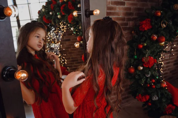 Beautiful little girl in a red dress in front of a mirror in loft room — ストック写真