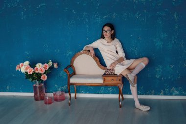 Ladylike woman in the pink dress is posing near the blue texture wall