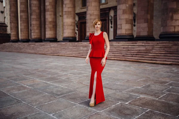 Uzun kırmızı elbiseli, yüksek topuklu ayakkabılı zarif bir kadın merdivenlerde oturuyor. — Stok fotoğraf
