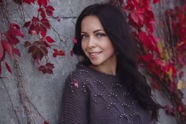 Girl on background wall with red autumn leaves.