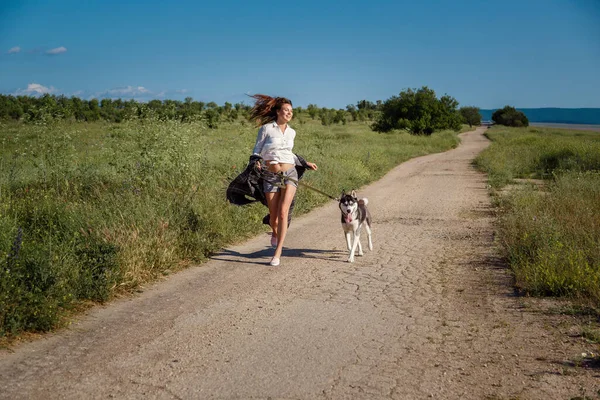 sport girl is running with a dog the siberian husky on the road. Happy woman concept. Wild in soul. Siberian husky favorite pet.
