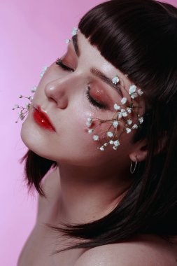 Taze, pürüzsüz bir teni, pembe arka planda çiçekli çıplak makyajı olan genç ve güzel bir kadının stüdyo güzelliği portresini kapat. Moda fotoğrafı.