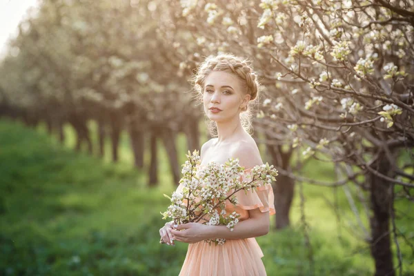 開花の庭の薄いドレスを着た金髪の女の子 女性の春のファッションの概念 若いモデルはカメラの表情を見る — ストック写真
