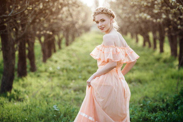 girl with blonde hair in a light dress in flowering garden. concept of female spring fashion. Young model looking at camera expressive.