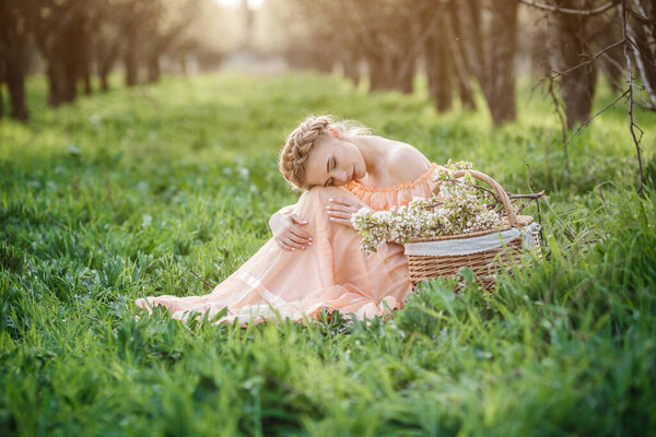 Girl with blonde hair in a light dress in flowering garden. concept of female spring fashion. Young model looking at camera expressive.