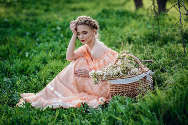 girl with blonde hair in a light dress in flowering garden. concept of female spring fashion. Young model looking at camera expressive.
