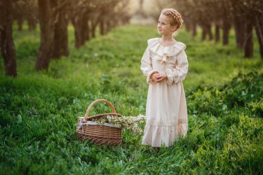 6-7 yaşlarında güzel bir kız, beyaz elbiseyle bahçede poz veriyor. Paskalya zamanı. Bahar ve sıcağı seviyor. Mutlu çocukluk, huzur ve mutluluk konsepti. Aromatik çiçekler ve antika mahsuller.