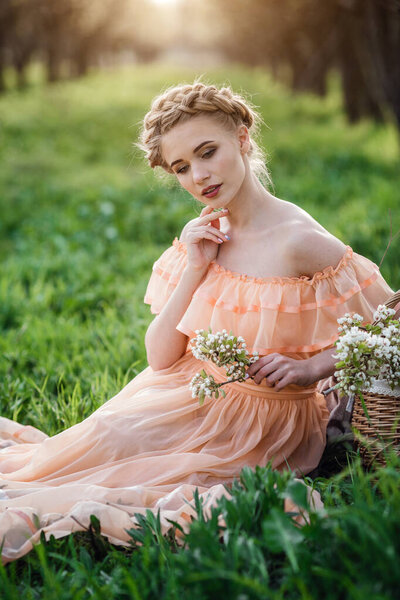 girl with blonde hair in a light dress in flowering garden. concept of female spring fashion. Young model looking at camera expressive.
