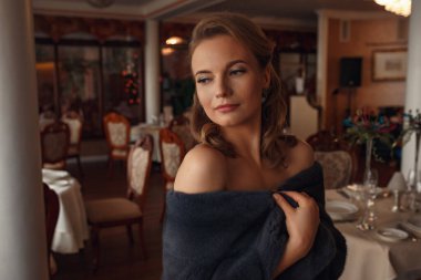 Teras restoranında bir etkinlik bekleyen güzel genç bir kadın. Şenlik ve etkinliklere hazırlanıyorum. Deniz manzaralı lüks bir elbise.