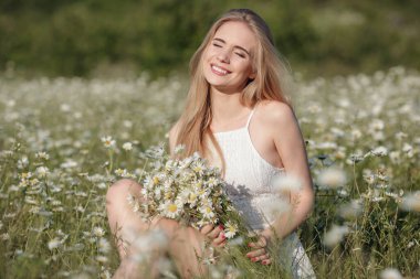 Resimli bir vadideki papatya tarlasında güzel bir genç kadın. Mutlu genç bayan ve bahar yeşili doğa, uyum kavramı. Kişisel bakım fikri, sağlıklı bir yaşam tarzı ve olumlu bir tutum.