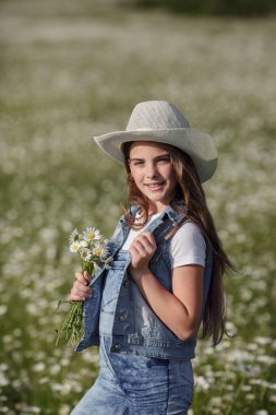 Papatya tarlasında baharın tadını çıkarıyor. Mutlu çocukluk kavramı ve fikri. Güneşli bir yaz gününde çayırda kot pantolon giyen genç.