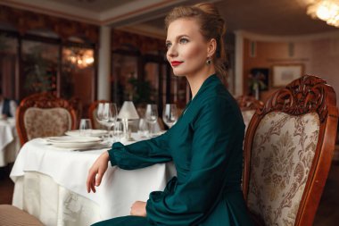 Teras restoranında bir etkinlik bekleyen güzel genç bir kadın. Şenlik ve etkinliklere hazırlanıyorum. Deniz manzaralı lüks bir elbise.