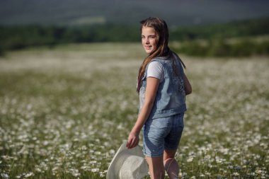 Papatya tarlasında baharın tadını çıkarıyor. Mutlu çocukluk kavramı ve fikri. Güneşli bir yaz gününde çayırda kot pantolon giyen genç.