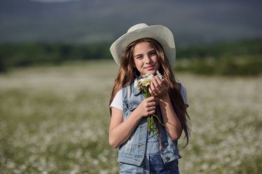 Papatya tarlasında baharın tadını çıkarıyor. Mutlu çocukluk kavramı ve fikri. Güneşli bir yaz gününde çayırda kot pantolon giyen genç.