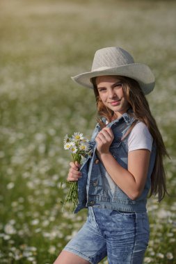 Papatya tarlasında baharın tadını çıkarıyor. Mutlu çocukluk kavramı ve fikri. Güneşli bir yaz gününde çayırda kot pantolon giyen genç.