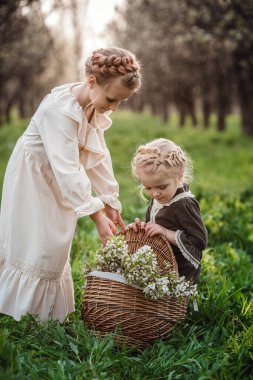 İki kız kardeş ya da kız arkadaş bahçede yürüyorlar, güzel klasik elbiselerle baharın tadını çıkarıyorlar. Arkadaş canlısı bir aile ve mutlu bir çocukluk fikri. Paskalya zamanı ve uyanma