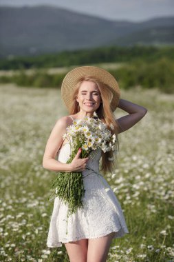 Resimli bir vadideki papatya tarlasında güzel bir genç kadın. Mutlu genç bayan ve bahar yeşili doğa, uyum kavramı. Kişisel bakım fikri, sağlıklı bir yaşam tarzı ve olumlu bir tutum.