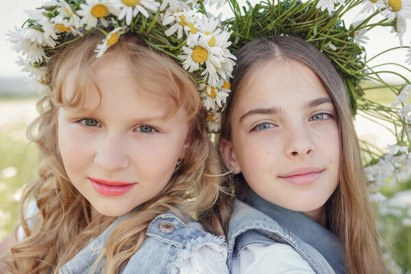 two cute teen girls in denim overalls walk in a daisy field. idea and concept of health, happy childhood, friendship
