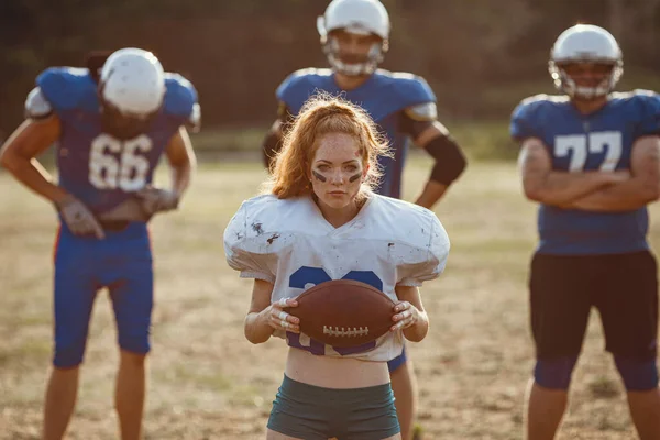 American football woman player in action on the stadium. little red-haired girl with freckles plays sports of large and strong men in football on the field at sunset