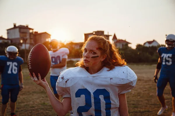 American football woman player in action on the stadium. little girl playing with big men in football on the field at sunset