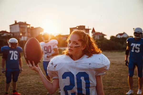American football woman player in action on the stadium. little girl playing with big men in football on the field at sunset