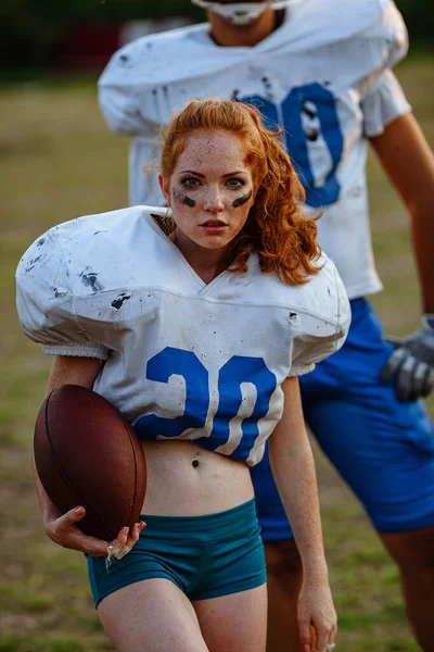 American football woman player in action on the stadium. little girl playing with big men in football on the field at sunset