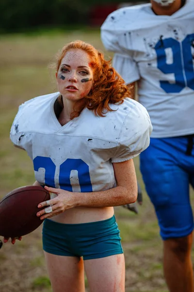 American football woman player in action on the stadium. little girl playing with big men in football on the field at sunset