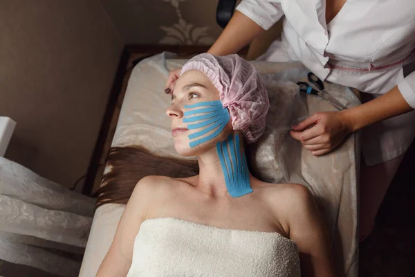 Face aesthetic taping. Facial skin care. Young woman lying with tape applications on face. Non-invasive anti-ageing lifting method for reduction of wrinkles on the forehead and the outer eye corners