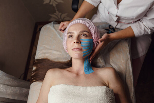 Лицо эстетическая лента. Уход за кожей лица. Молодая женщина лежит с приложениями на лице. Неинвазивный метод подъема против старения для уменьшения морщин на лбу и наружных углах глаз
