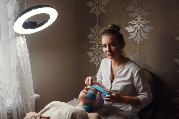 女性美容师在家里为躺在桌子上的病人做面部录音 理疗和美容程序 非手术性皮肤更新的方法 面部皮肤治疗 — 图库照片