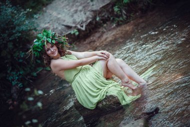 Yeşil elbiseli güzel bir kadın ve güneşli bir ormanda çelenk. Yaz ortası ya da Dünya Günü 'nde seremoni. Parfüm fikri ve konsepti, peri masalları ve mutluluk