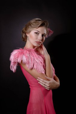 Siyah arka planda pembe tüylü güzel bir elbise giyen sarışın kız. Hoş görünümlü beyaz kadın kameraya mutlu bir şekilde bakıyor, duygusal bir portre.
