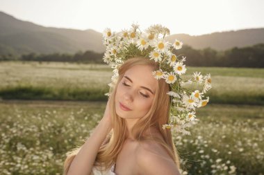 Çayırda güzel sarışın bir kadının portresi kameraya bakıyor ve bahar akşamının tadını çıkarıyor. Beyaz kadın parkta rahatlıyor, papatya dışarıda fotokopi odası var.