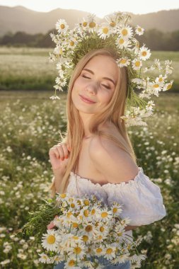 Çayırda güzel sarışın bir kadının portresi kameraya bakıyor ve bahar akşamının tadını çıkarıyor. Beyaz kadın parkta rahatlıyor, papatya dışarıda fotokopi odası var.