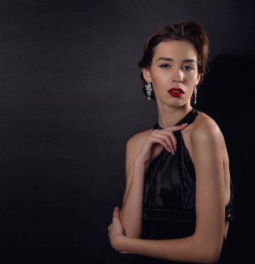 Zarif dalgalı saç stili, parlak makyajlı güzel bir kadın. Siyah elbise giyen, siyah arka planda yalnız poz veren moda esmeri. Göz kapağı oklarında ve kırmızı rujda klasik makyaj.