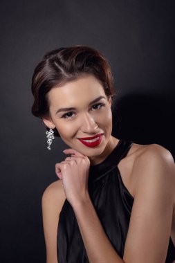 Zarif dalgalı saç stili, parlak makyajlı güzel bir kadın. Siyah elbise giyen, siyah arka planda yalnız poz veren moda esmeri. Göz kapağı oklarında ve kırmızı rujda klasik makyaj.