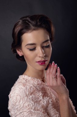 Temiz makyajlı ve siyah arka planda pembe kazaklı esmer bir kadının hassas portresi. Güzel saç stili, sağlıklı görünüyor.