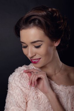 Temiz makyajlı ve siyah arka planda pembe kazaklı esmer bir kadının hassas portresi. Güzel saç stili, sağlıklı görünüyor.