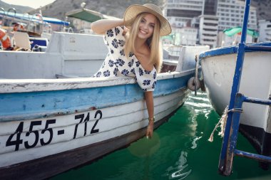 Güzel, modaya uygun bir genç kız deniz kenarında yürüyor, yatları ve tekneleriyle rıhtımda. Boş zaman, tatil köyü, güzellik, moda, gençlik kavramı