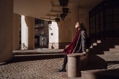 Avrupa 'nın caddesinde poz veren gri ceketli, kırmızı deri çantalı, mutlu, mutlu, mutlu, neşeli, neşeli bir kızın açık hava sonbahar portresi. Kopyala, metin için boşluk