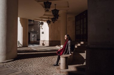 Avrupa 'nın caddesinde poz veren gri ceketli, kırmızı deri çantalı, mutlu, mutlu, mutlu, neşeli, neşeli bir kızın açık hava sonbahar portresi. Kopyala, metin için boşluk