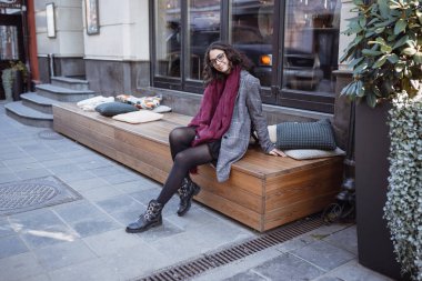 Avrupa 'nın caddesinde poz veren gri ceketli, kırmızı deri çantalı, mutlu, mutlu, mutlu, neşeli, neşeli bir kızın açık hava sonbahar portresi. Kopyala, metin için boşluk