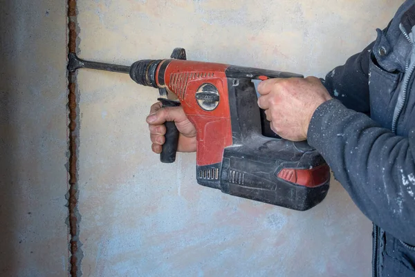 Worker using a jackhammer to drill into wall for electricity installation, on construction site