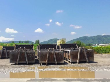 Üç kömür konteynırı, arkasında mavi gökyüzü olan kömür deposu.