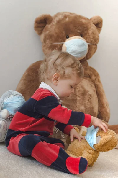 Child playing with his sick teddy bears wearing medical mask against viruses. Role playing, child playing doctor with plush toy. Children and illness concept.