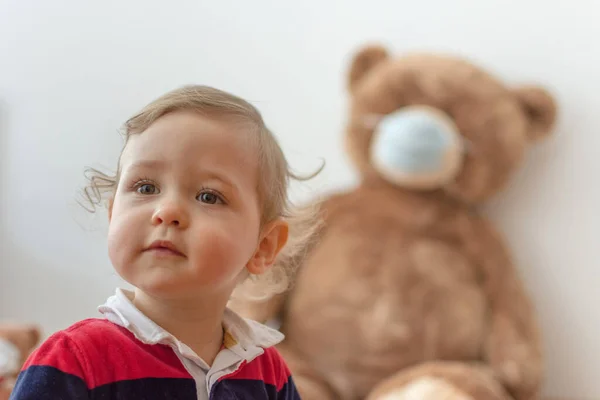 Child playing with his sick teddy bears wearing medical mask against viruses. Role playing, child playing doctor with plush toy. Children and illness concept.