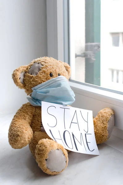 Sick teddy bear in home quarantine wearing a medical mask against viruses during coronavirus and flu outbreak, with the advice to stay home.