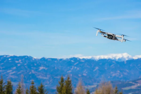 背景に青い空を飛ぶ写真カメラと美しい山の風景を持つ白いドローン — ストック写真